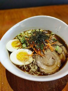 Ramen bowl featuring soft-boiled eggs, sliced pork, green onions, and seaweed in savory broth.